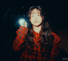 a woman in a red plaid shirt is holding a flashlight and the letters ms are on the bottom right