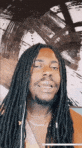 a man with long black dreadlocks and a beard is smiling in front of a painting .