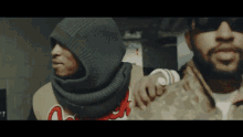 two men are standing next to each other and one of them is wearing a hood