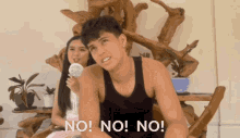 a man in a black tank top is sitting in front of a woman holding a microphone and says no