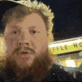 a man with a beard is standing in front of a waffle house sign