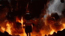 a man in a red shirt is standing in front of a large explosion .