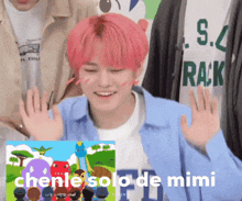 a boy with pink hair is smiling and raising his hands in front of a picture of a cartoon .