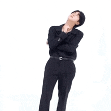 a man in a black shirt and pants is standing in front of a white background and pointing at something .