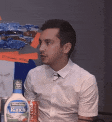 a man in a white shirt is sitting next to a bottle of ranch dressing