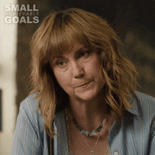 a woman wearing a blue striped shirt and a necklace with small achievable goals written on the bottom