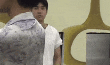 a man in a white shirt is standing next to another man in a floral shirt .
