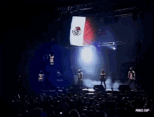 a group of people standing on a stage with a mexican flag in the background