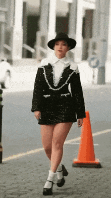 a woman wearing a black and white dress and a hat walks down a street