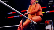two wrestlers are wrestling in a ring with a referee in the background .