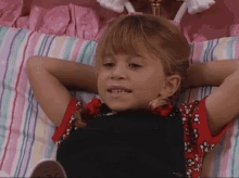 a little girl is laying on a bed with her hands behind her head and making a funny face .