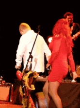 a woman in a red dress is dancing on stage with a man playing a guitar