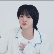 a young man with black hair is wearing a white jacket
