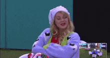 a woman wearing a hat and a blue sweater is sitting in a chair .