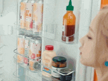a woman is looking into a refrigerator filled with bottles and cans