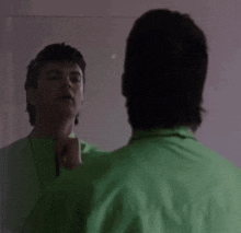 a man in a green jacket is standing in front of a wall .