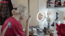 a woman in a red shirt is applying makeup in front of a mirror with the word seventeen on the bottom