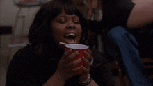 a woman is drinking from a red cup and smoking a cigarette