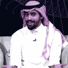 a man wearing a head scarf and a white shirt has a microphone on his neck