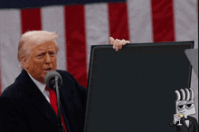 donald trump holds a sign that says tanssj in front of an american flag