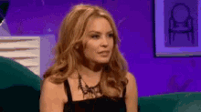 a woman in a black dress is sitting on a couch looking at the camera .