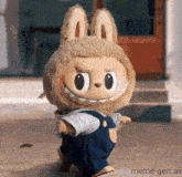 a stuffed animal wearing overalls and a bunny hat is standing on a sidewalk .