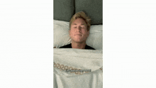 a young man wearing a black t-shirt is sitting on a bed making a funny face .