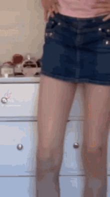 a woman is standing in front of a white dresser wearing a denim skirt .