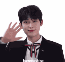 a young man wearing a suit and bow tie is waving his hand