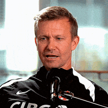 a man speaking into a microphone wearing a black shirt that says circus