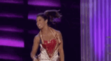 a woman is dancing on a stage in front of a purple background .
