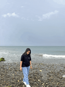 a woman standing on a rocky beach with the ocean behind her