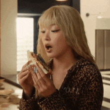 a woman wearing a leopard print sweater is eating a sandwich
