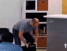 a man in a blue shirt is kneeling down in front of a counter that says ' t ' on it