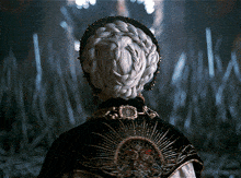 a woman with a braided hairstyle is wearing a black cape with a crown on the back