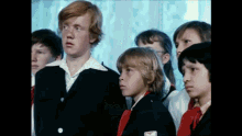 a group of children are standing in a room and one of them has a red bow tie
