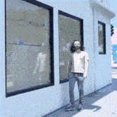 a man with long hair is standing in front of a building with two windows