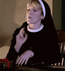 a nun is smoking a cigarette while sitting at a table in a chair .