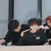 a group of young men are sitting at a table and one of them is wearing a black shirt with the word ni on it .