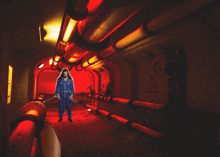 a man in a blue jumpsuit is standing in a hallway with red pipes