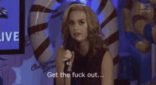 a woman is holding a microphone and saying get the fuck out .