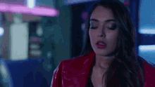 a woman in a red leather jacket is standing in front of a neon sign .