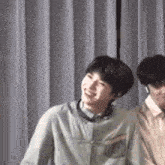 two young men are standing next to each other in front of a curtain .