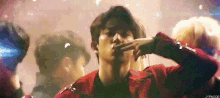 a man in a red jacket is smoking a cigarette in a crowd of people .