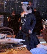 a woman in a black dress and hat is standing in a room