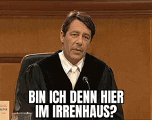 a man in a judge 's robe is sitting in front of a microphone and says bin ich denn hier im irrenhaus