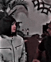 a woman in a white jacket is talking to a man in a room