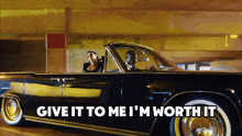 a man and a woman in a black car with the words give it to me i 'm worth it