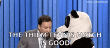 a man in a suit and tie is sitting next to a stuffed panda bear and says the tennis match is good .