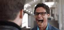 a man with glasses is laughing while looking at himself in the mirror .